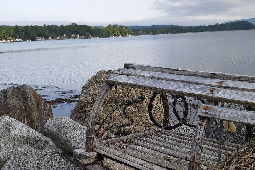 A wooden lobster trap on the rocks at the water's edge